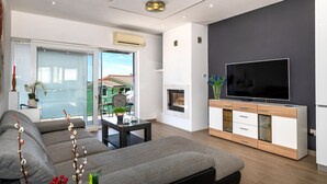 Una sala de estar moderna con un sofá, televisión, chimenea y un balcón con vistas a casas.