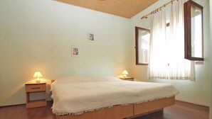 A bedroom with a wooden bed, two bedside tables with lamps, a window with curtains, and a small picture on the wall. - Holiday apartment with air conditioning (Pula)