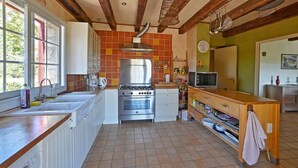 Een keuken met een fornuis, oven en magnetron, houten balken in het zicht en een raam met uitzicht op groen.