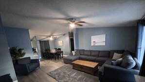 En moderne stue med en grå sofa, et træbord og et spiseområde med bord og stole.