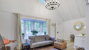 A well-lit room with a large window, a sofa, a coffee table, and a chandelier. - Walk to Lake & Pool! Hot Tub, Air Hockey, Pool Table, Boat Rental, BBQ, Fire Pit (Pocono Lake)