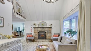 A cozy living room with a stone fireplace, a sofa, a coffee table, and a dining area in the background. - Walk to Lake & Pool! Hot Tub, Air Hockey, Pool Table, Boat Rental, BBQ, Fire Pit (Pocono Lake)