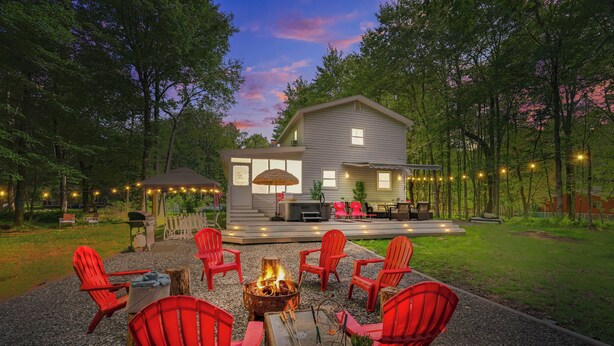 A backyard with a fire pit, red Adirondack chairs, and a house with a deck. - Walk to Lake & Pool! Hot Tub, Air Hockey, Pool Table, Boat Rental, BBQ, Fire Pit (Pocono Lake)