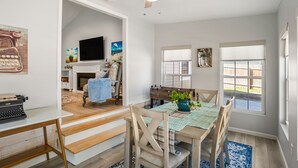 A dining area with a wooden table, chairs, and a blue rug. There is a fireplace with a blue towel and a television in the background. - Modern home near historic downtown and Port Royal town beach.  Pet friendly! (Beaufort)