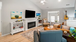 Een woonkamer met een open haard, een televisie, een gitaar en een eethoek.