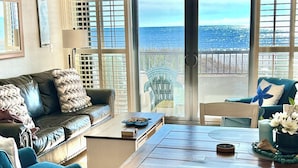 A living room with a wooden dining table, a leather sofa, and a view of the ocean through large sliding glass doors. - Two of the three bedrooms have ocean front balconies! (North Myrtle Beach)