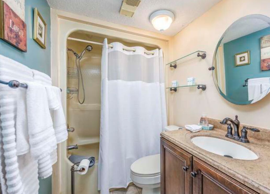 A bathroom with a shower, toilet, sink, and towel rack.