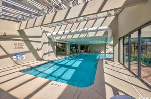 An indoor swimming pool with safety signs, a covered area, and a view of the outside.
