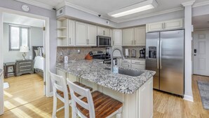 A modern kitchen with white cabinets, a granite countertop, stainless steel appliances, and a breakfast bar with two chairs. - Two of the three bedrooms have ocean front balconies! (North Myrtle Beach)