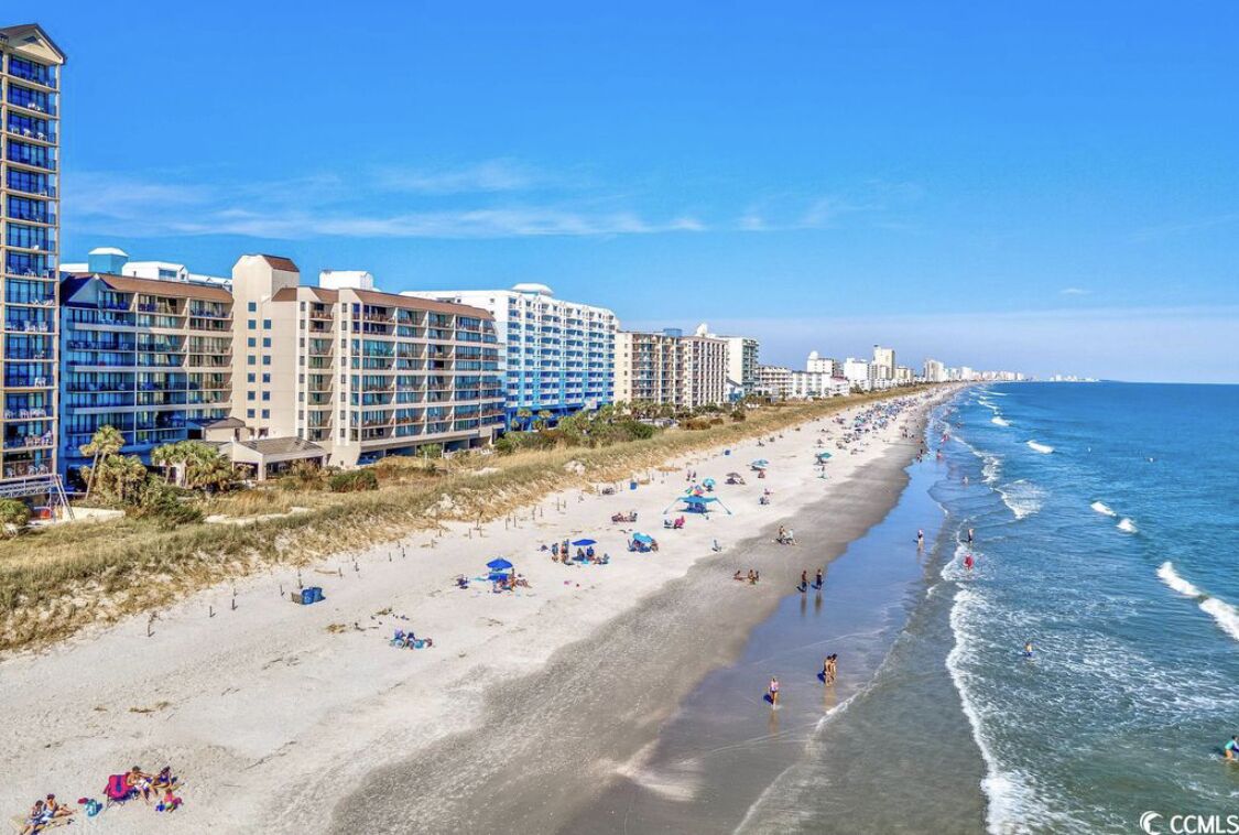 A beachside hotel with multiple floors, a sandy beach, and ocean views.