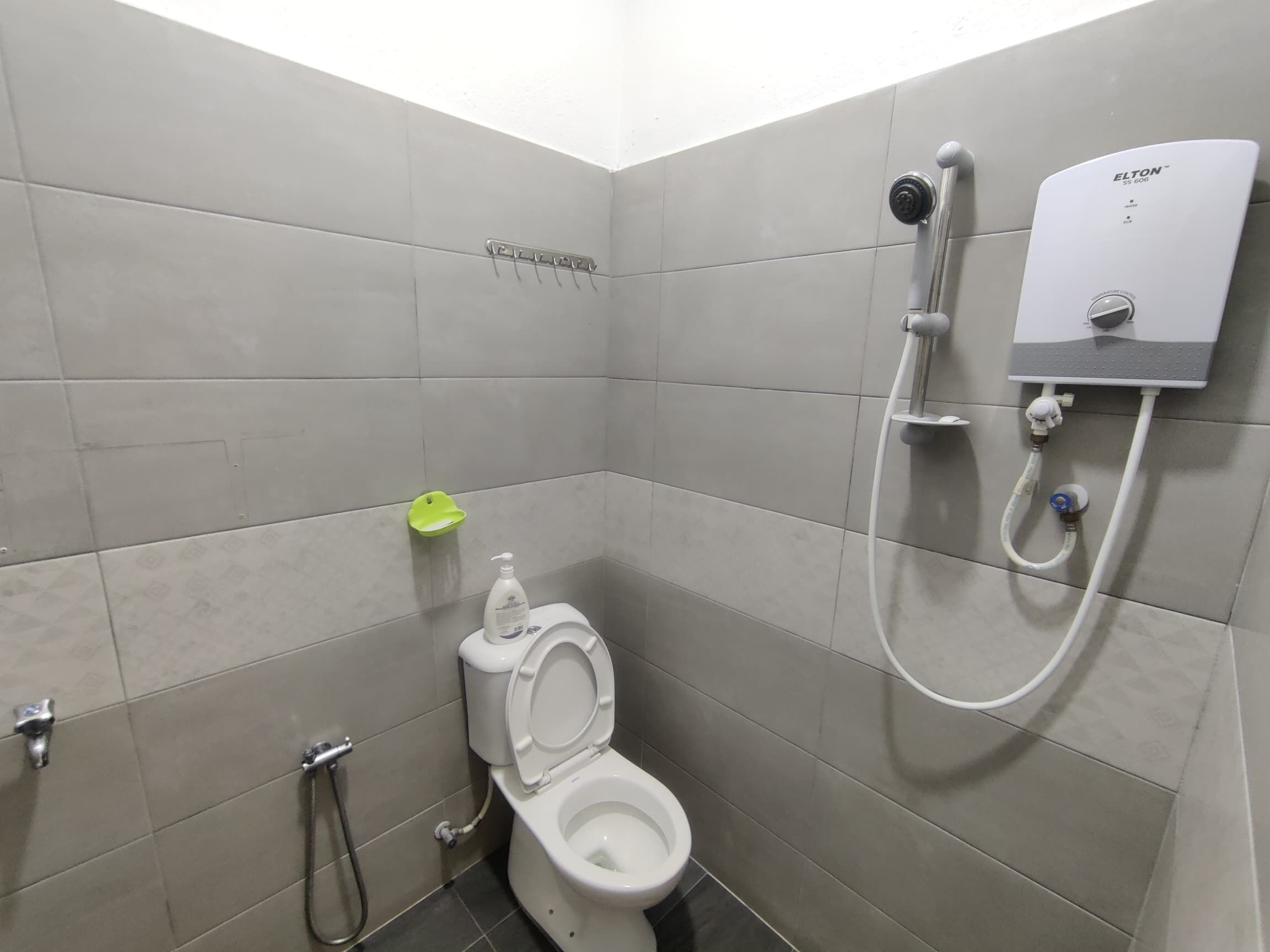 A small, modern bathroom with a toilet, a shower unit, and a green soap dish.