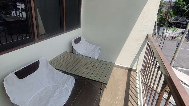 A balcony with a metal table and two white chairs, a window with black curtains, and a view of the street below. - CLP Home near Sri Muniswarar Temple 2 (Perai)