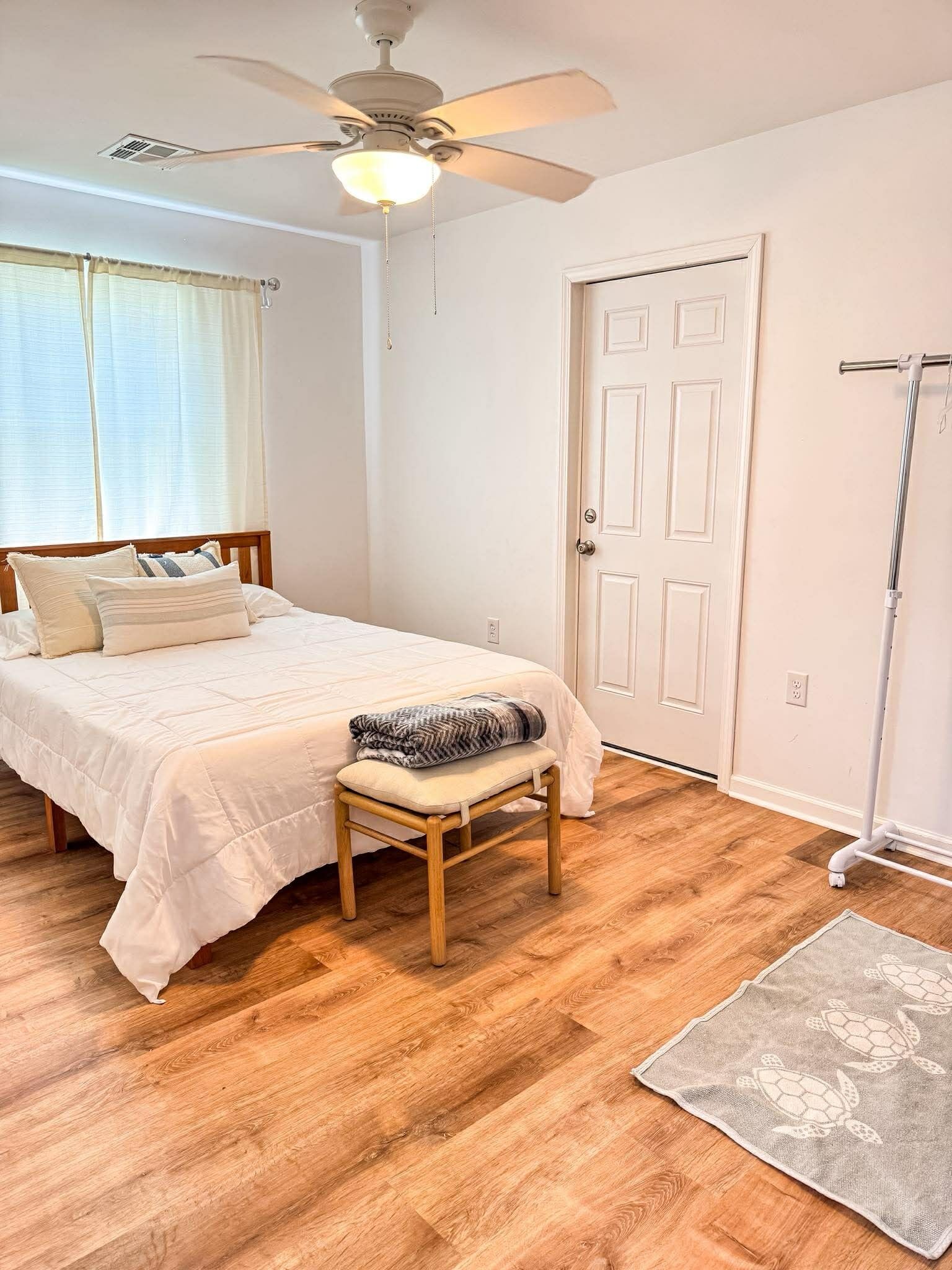A bedroom with a bed, a ceiling fan, a door, and a floor lamp.