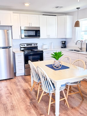 A modern kitchen with white cabinets, stainless steel appliances, a dining table with chairs, and a hanging light fixture.