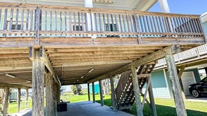 Uma área externa coberta com um deck de madeira, piso de concreto e vista para uma casa ao fundo.