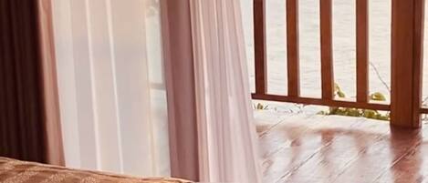 Une chambre avec un plancher en bois, un lit recouvert d’une couvre-lit à motifs et une vue sur la mer depuis le balcon.