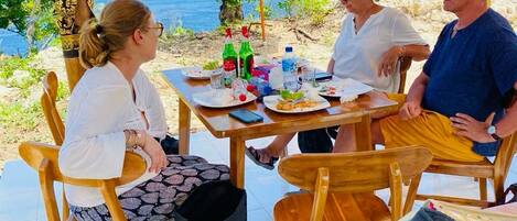 A group of people seated at a wooden table outdoors with a view of the sea.