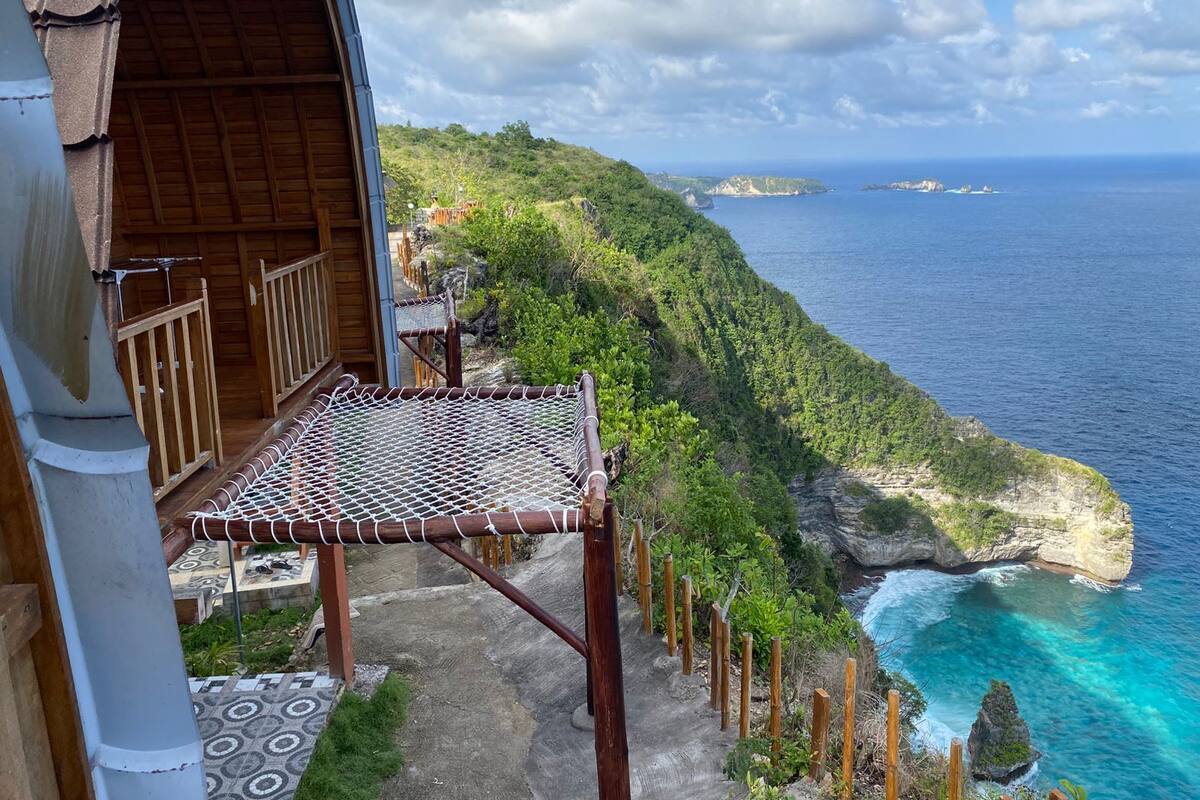 A wooden balcony with a netted table, overlooking a coastal cliff and ocean.
