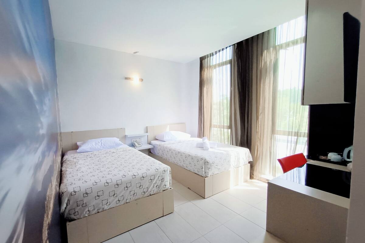 Habitación de hotel con dos camas, un escritorio pequeño y una ventana con cortinas.