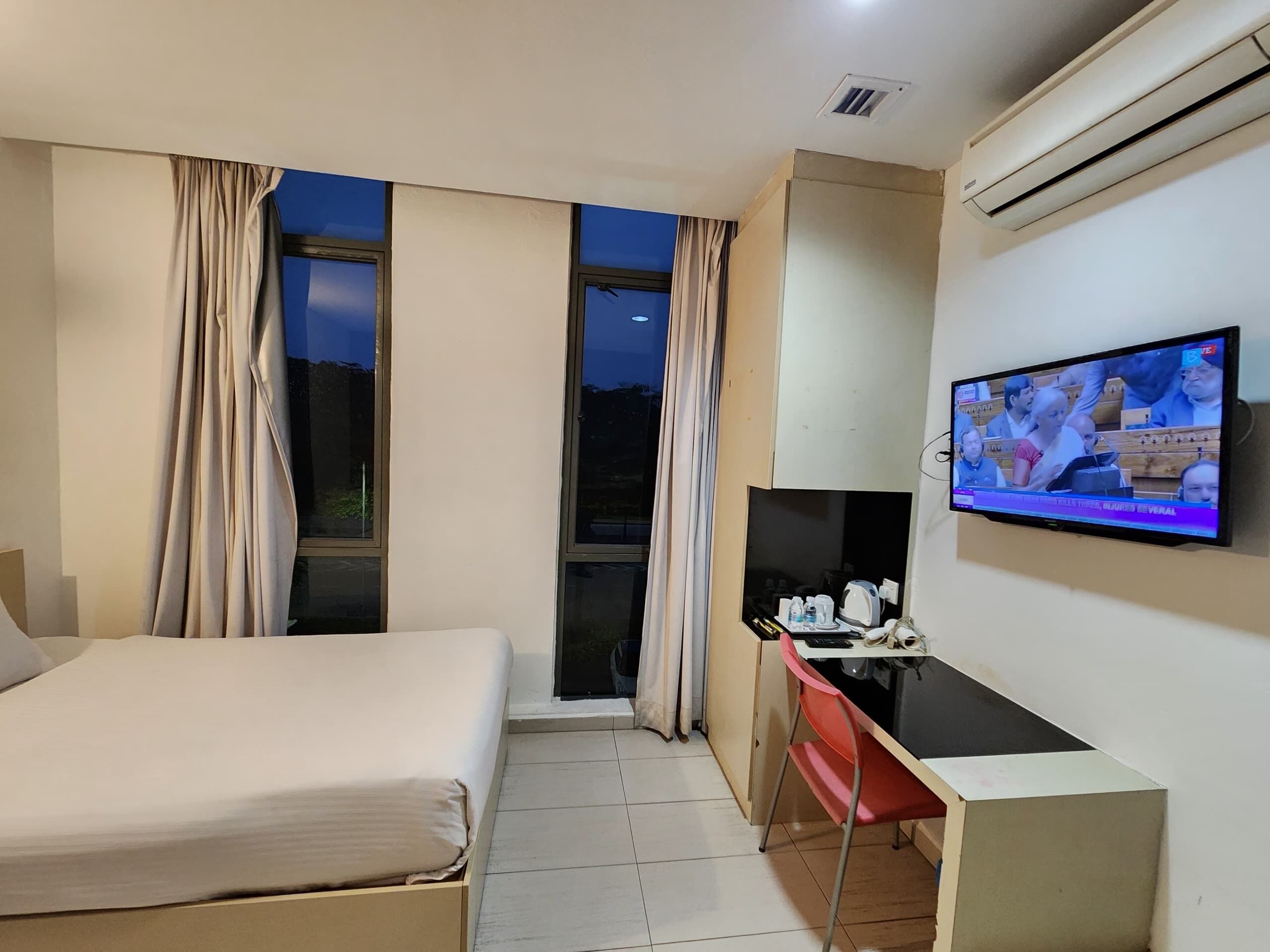 Ein Hotelzimmer mit Bett, Schreibtisch, Fernseher und großen Fenstern.