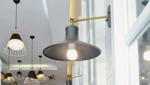 Interior moderno com luminárias pendentes, escada de madeira e vista para o exterior através de grandes janelas.