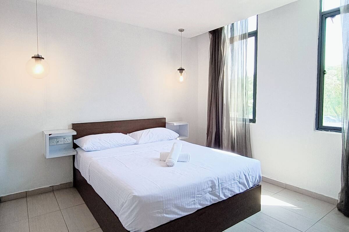 Una habitación de hotel moderna con una cama grande, una mesita de noche y dos lámparas colgantes.