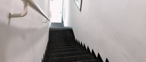 A stairway with black steps and white walls, leading to a door with a sign reading "KELUAR".