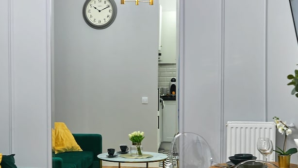 A modern living room with a green sofa, a round coffee table, a clear chair, and a large mirror reflecting the room.