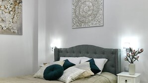 A neatly arranged bedroom with a large bed, a bedside table, a decorative wall piece, and a hanging light fixture.