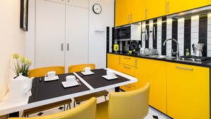 A modern kitchen with yellow cabinets, a black countertop, and a dining area with a table set for four. - At the Fountain Apartment (Warszawa)