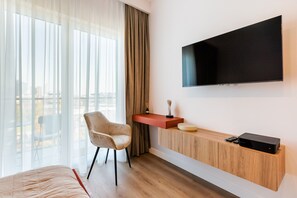 Ein Hotelzimmer mit Bett, Schreibtisch mit Stuhl, einem an der Wand montierten Fernseher und Blick ins Freie.