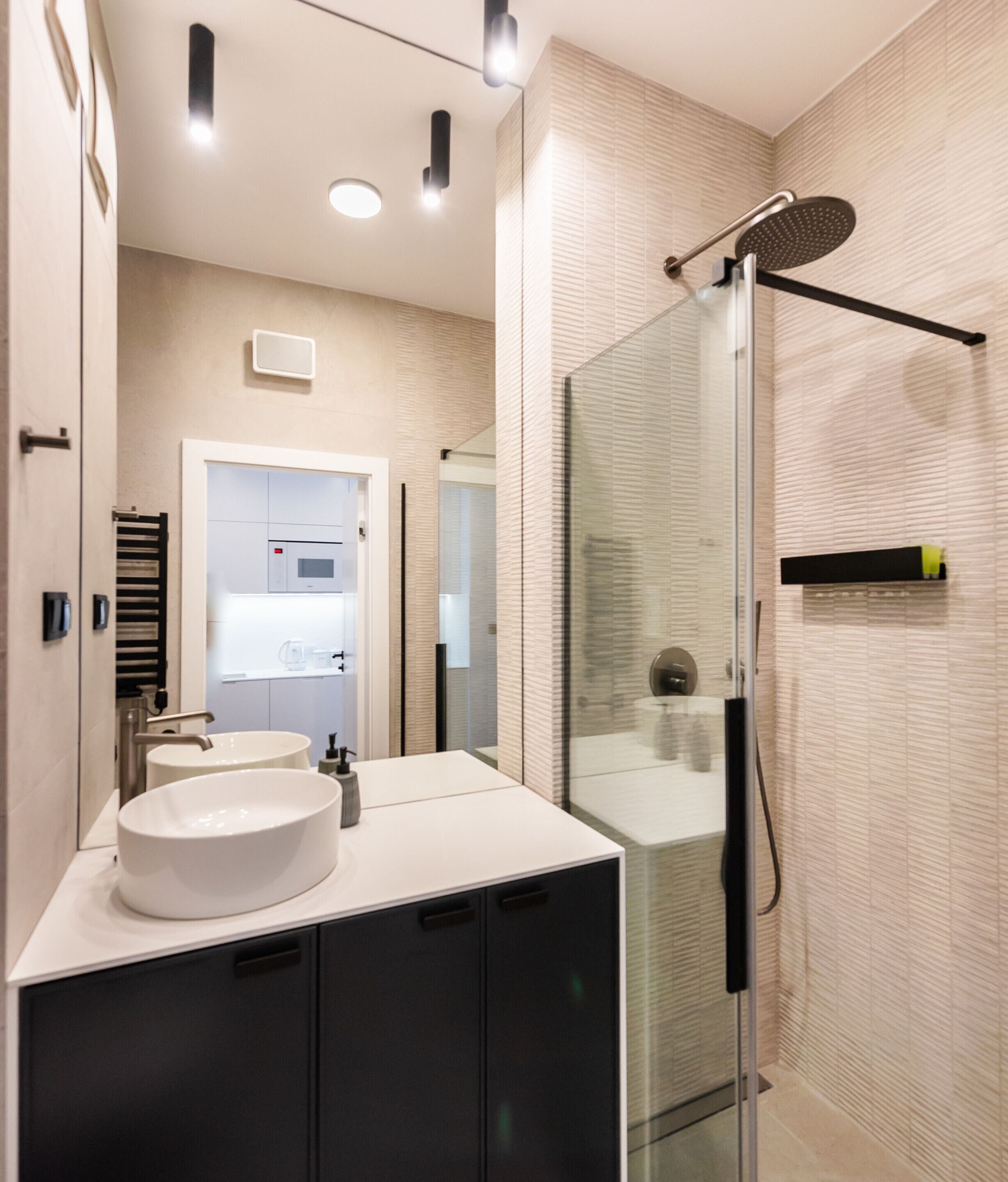 A modern bathroom with a glass shower enclosure, a white sink, and a black cabinet.