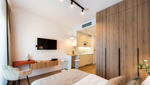 A modern hotel room with a bed, a desk, a chair, a TV, and a kitchenette.