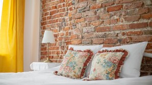 A hotel room with a brick wall, a bed with white bedding, and floral pillows.