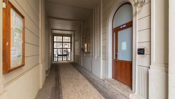 A corridor with a wooden door, a bulletin board, and a window at the end.