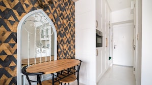 A hallway with a geometric patterned wall, a wooden table with chairs, and white cabinets with gold handles. - City Centre All In One Apartment (Warszawa)