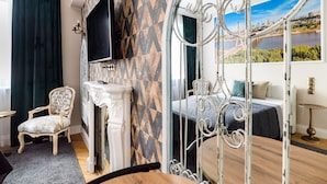 A room with a bed, a TV, a chair, and a view of a cityscape through a window. - City Centre All In One Apartment (Warszawa)