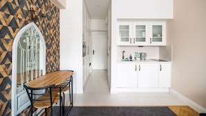 A modern kitchen with white cabinetry, a dining area with a wooden table and chairs, and a patterned wall. - City Centre All In One Apartment (Warszawa)