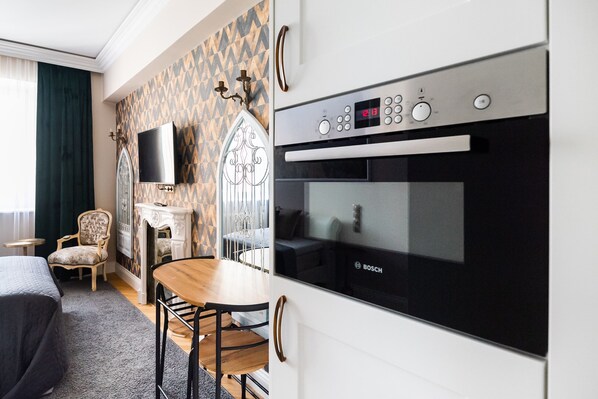 Een hotelkamer met een moderne keuken, inclusief een Bosch oven, een eethoek met een houten tafel en stoelen, een aan de muur bevestigde televisie en een decoratieve open haard.