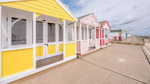 Une rangée de cabanes de plage aux façades blanches et jaunes, chacune dotée d’un petit porche et de fenêtres.