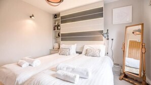 Un lit bien fait, avec du linge de lit et des serviettes blanches, une lampe de chevet, un miroir et une étagère avec des livres et des objets décoratifs.