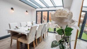 Un coin repas avec une table dressée pour quatre personnes, une rose blanche dans un vase et une vue sur l’extérieur grâce à de grandes fenêtres.