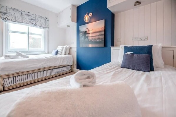 Un dormitorio con dos camas, un ventanal grande, un cuadro colgado en la pared y una pared de acento azul.