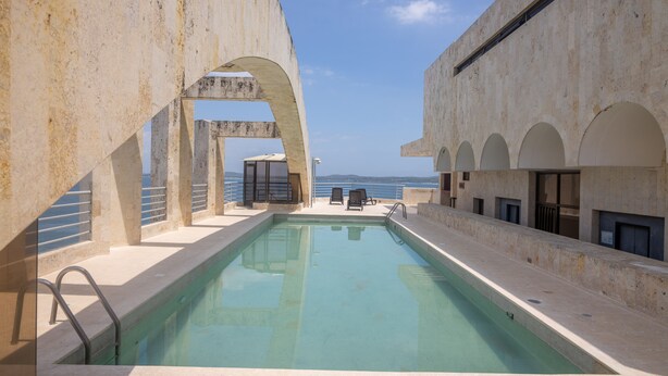 A swimming pool with a view of the sea, surrounded by a concrete structure with arches and a balcony.
