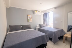 A hotel room with two beds, a small wooden table, a window with curtains, an air conditioning unit, and a framed picture on the wall. - Penthouse con Piscina Privada El Laguito (Cartagena)