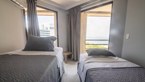 A hotel room with two beds, a small stool, and a view of the city and water.