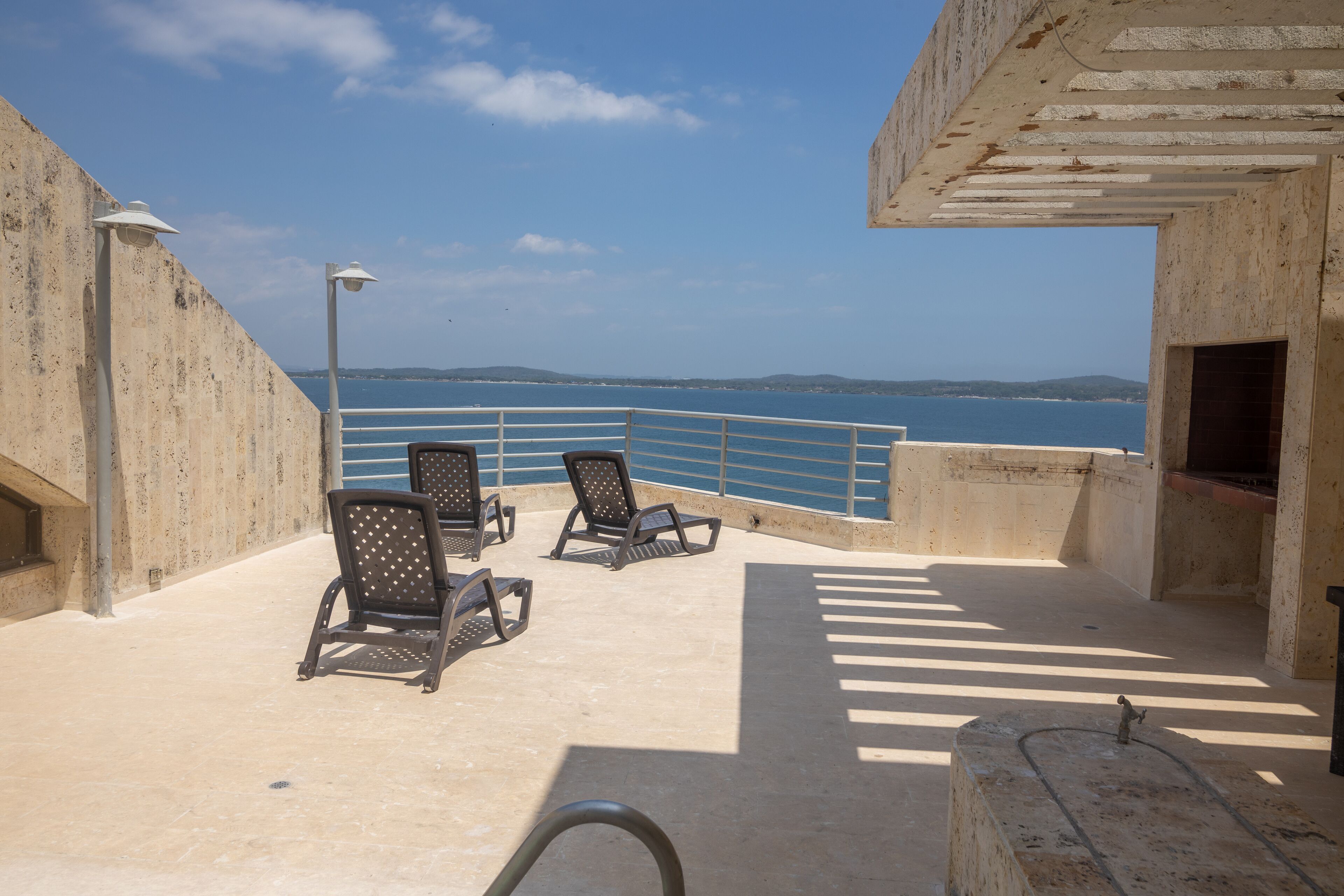 A rooftop terrace with two lounge chairs, a metal railing, and a view of the sea.