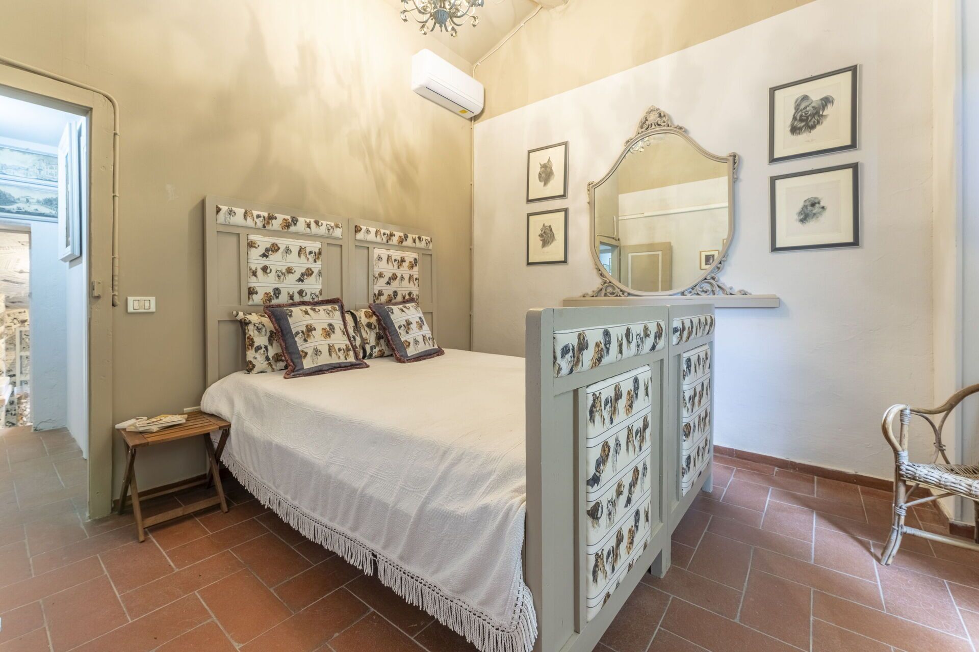 Un dormitorio con cama, mesita de noche, espejo y una pared decorada con cuadros.