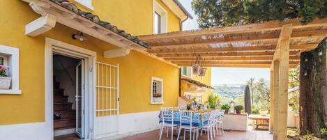 A yellow building with a covered patio, a staircase, and a view of the countryside.