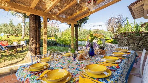 An outdoor dining area with a long table set for multiple guests, surrounded by greenery and a stone wall. - Wonderful private villa with A/C, private pool, WIFI, TV, pets allowed and panoramic view (Cantagrillo-casalguidi)